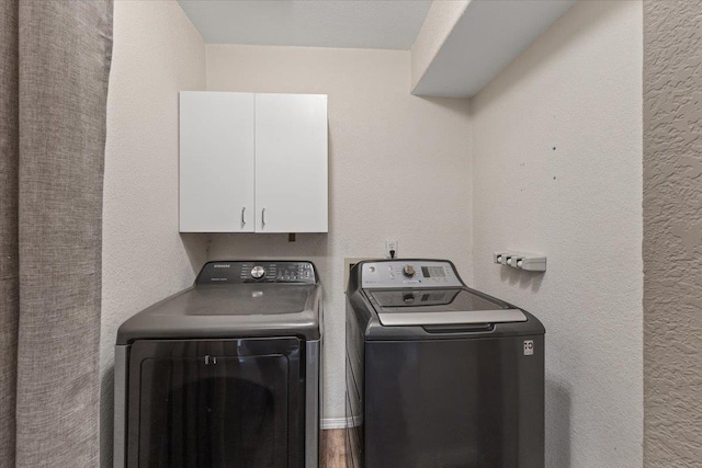 clothes washing area featuring cabinet space, a textured wall, and washer and clothes dryer