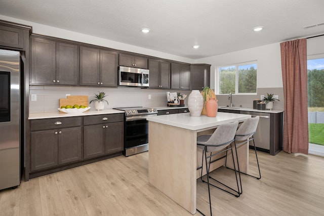 kitchen featuring dark brown cabinets, a breakfast bar, light wood-style floors, stainless steel appliances, and visible vents