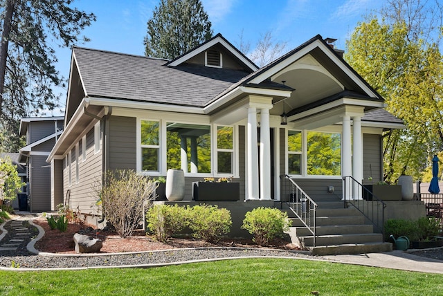 view of front of home featuring roof with shingles, covered porch, and a front lawn