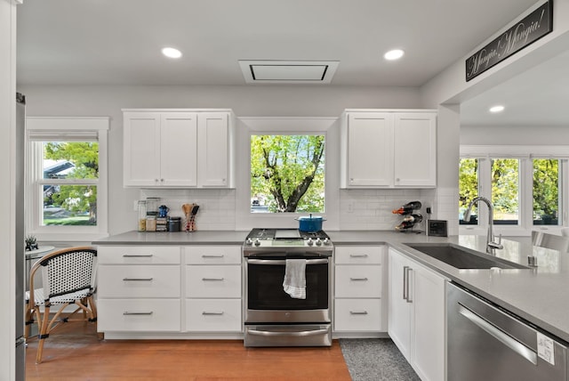 kitchen with a sink, backsplash, white cabinets, and stainless steel appliances