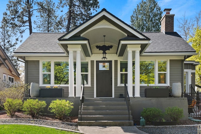 ranch-style home featuring a shingled roof, covered porch, and a chimney