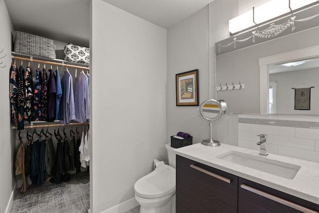 bathroom with vanity, toilet, baseboards, tasteful backsplash, and a spacious closet