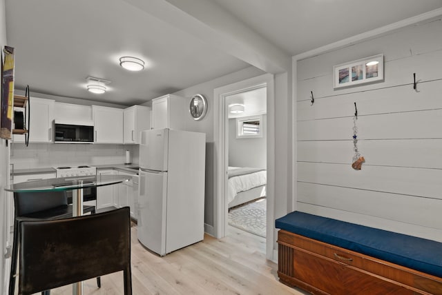 kitchen with range with electric stovetop, white cabinets, freestanding refrigerator, stainless steel microwave, and light wood-style flooring