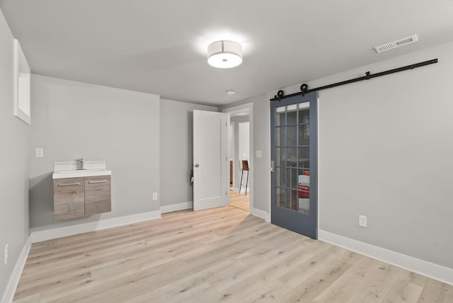 unfurnished bedroom featuring visible vents, a barn door, light wood finished floors, and baseboards