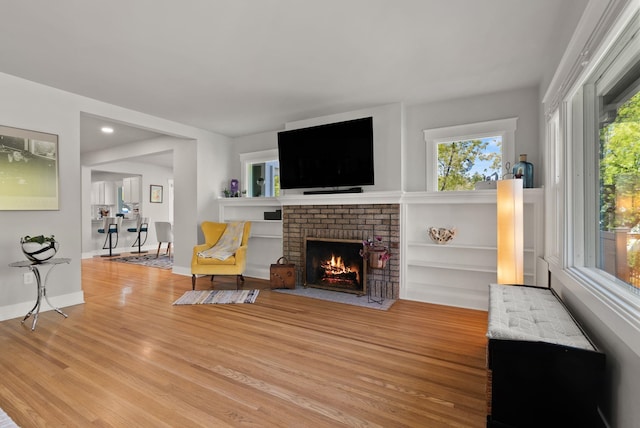 living area with a brick fireplace, baseboards, and light wood finished floors