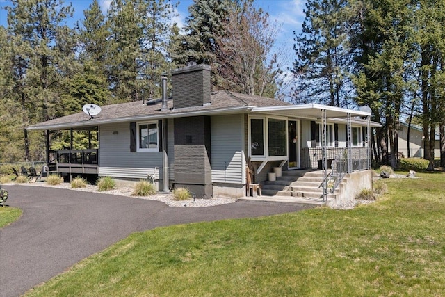 view of front of home with covered porch, a chimney, and a front lawn