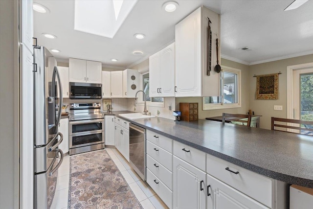 kitchen with appliances with stainless steel finishes, tasteful backsplash, a sink, ornamental molding, and white cabinetry