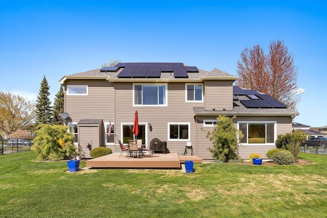 rear view of property featuring a lawn, roof mounted solar panels, a wooden deck, and fence