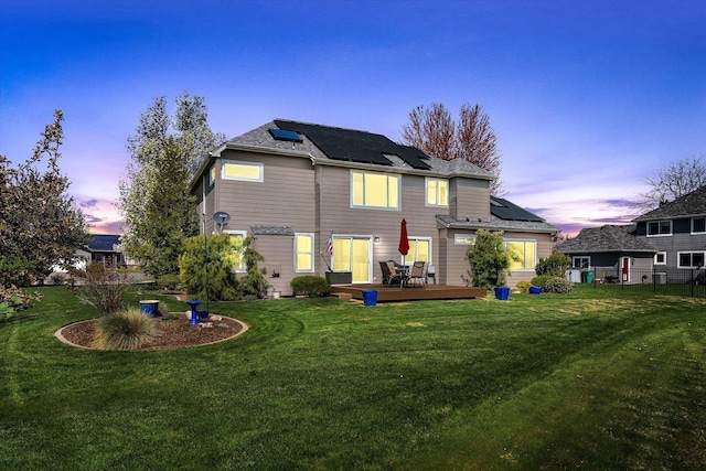 rear view of house featuring a yard, a wooden deck, and roof mounted solar panels