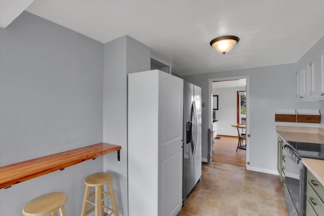 kitchen featuring wood counters, baseboards, a kitchen bar, stainless steel refrigerator with ice dispenser, and dishwashing machine
