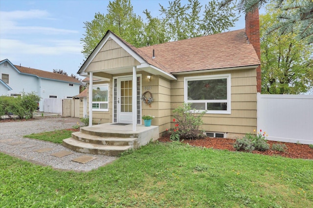 bungalow featuring roof with shingles, fence, a chimney, and a front yard