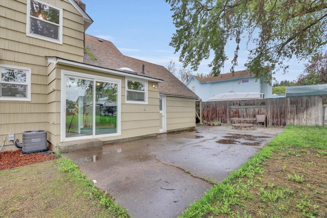 rear view of house featuring cooling unit, roof with shingles, a patio area, and fence