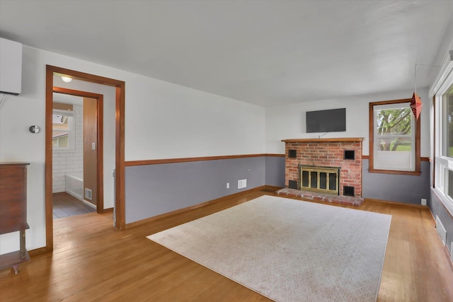 unfurnished living room featuring baseboards, a brick fireplace, wood finished floors, and visible vents
