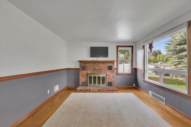unfurnished living room featuring a brick fireplace, visible vents, and wood finished floors
