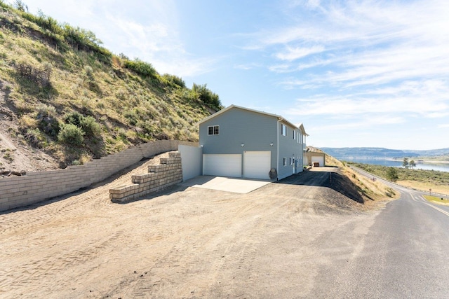 view of home's exterior featuring a garage, dirt driveway, and a water view