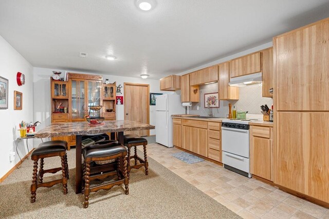 815 E Shelter Ln, Deer Park, WA 99006 - kitchen featuring white appliances, under cabinet range hood, a sink, light brown cabinetry, and a breakfast bar
