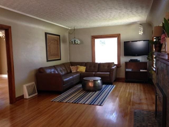 living room with a fireplace, a textured ceiling, baseboards, wood finished floors, and visible vents