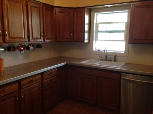 kitchen with brown cabinets, a sink, tile patterned flooring, light countertops, and stainless steel dishwasher