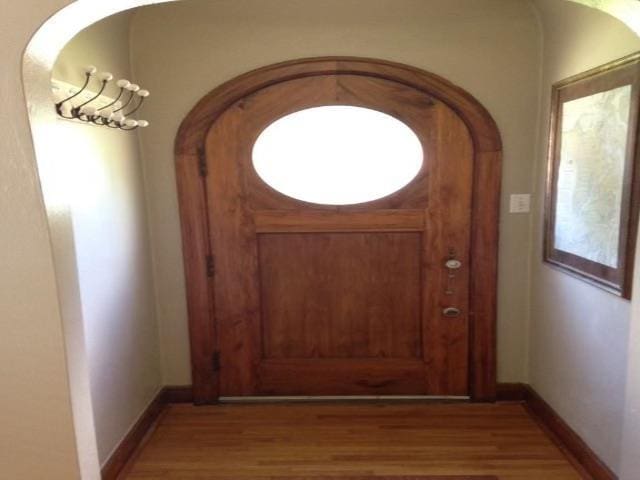 doorway to outside with arched walkways, baseboards, and wood finished floors