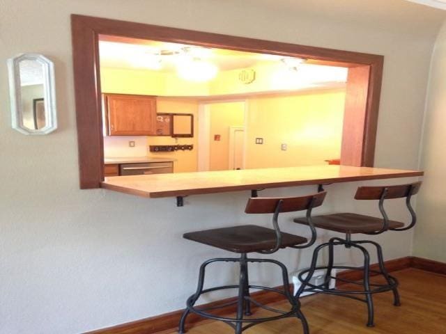 kitchen featuring wood finished floors, a breakfast bar, baseboards, brown cabinets, and dishwasher