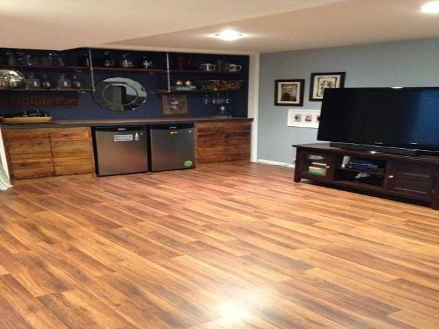 bar featuring wood finished floors, refrigerator, baseboards, a bar, and dishwasher