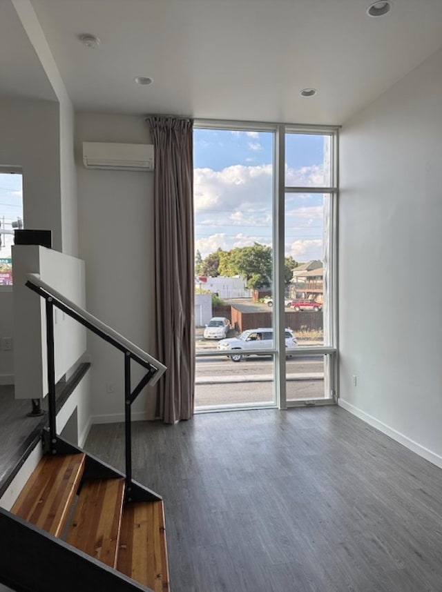 interior space with an AC wall unit, baseboards, a wall of windows, and wood finished floors