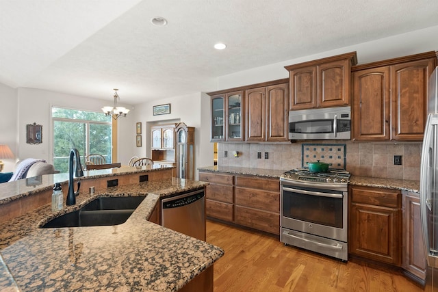 kitchen with an inviting chandelier, a sink, light wood-style floors, stainless steel appliances, and decorative backsplash