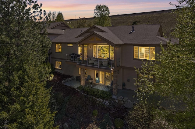 back of property at dusk with a patio, a shingled roof, and a deck
