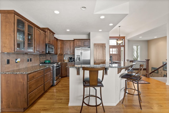 kitchen with stainless steel appliances, recessed lighting, light wood-type flooring, a kitchen bar, and glass insert cabinets