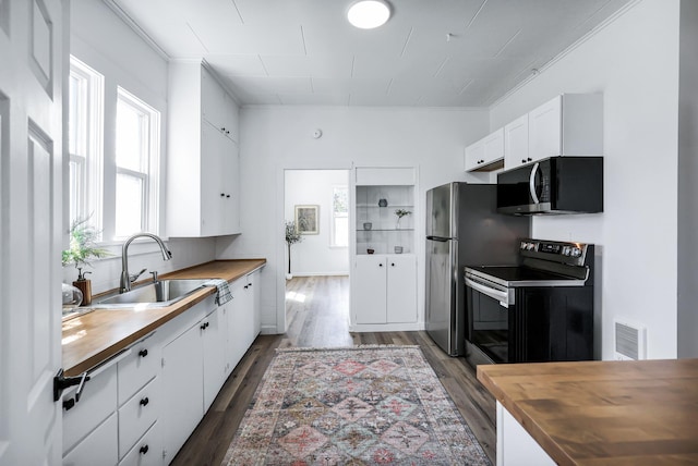 kitchen with a sink, wooden counters, range with electric cooktop, and visible vents