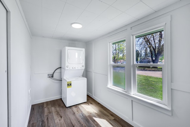 clothes washing area with laundry area, stacked washer and clothes dryer, baseboards, and wood finished floors