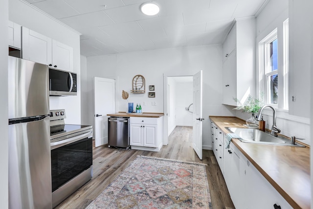 kitchen with white cabinets, a sink, light wood-style floors, wood counters, and stainless steel appliances