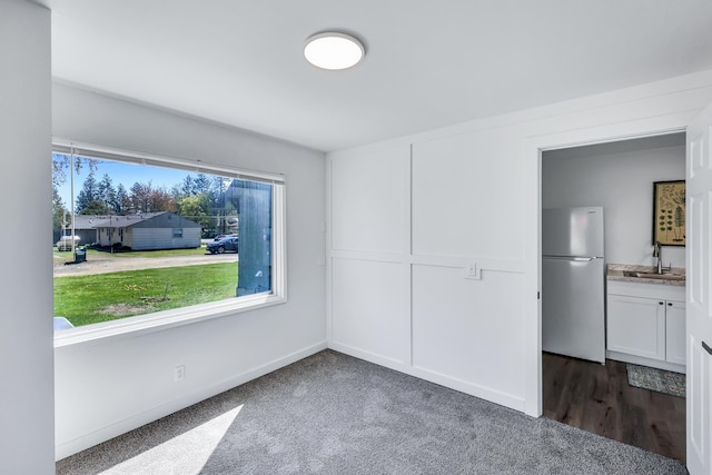 unfurnished room featuring a sink, baseboards, and dark carpet