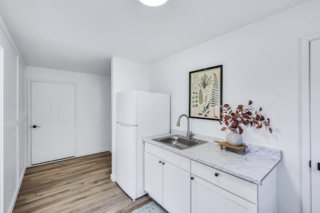 kitchen featuring white cabinets, a sink, freestanding refrigerator, baseboards, and light wood-type flooring