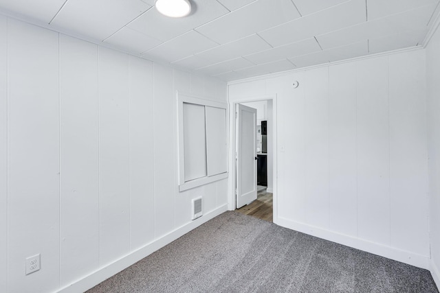 carpeted spare room featuring visible vents and a decorative wall