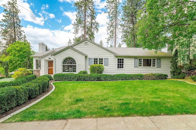 ranch-style house featuring a chimney, brick siding, and a front yard