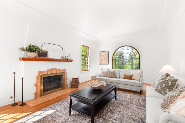living room with baseboards, visible vents, a fireplace with flush hearth, and wood finished floors