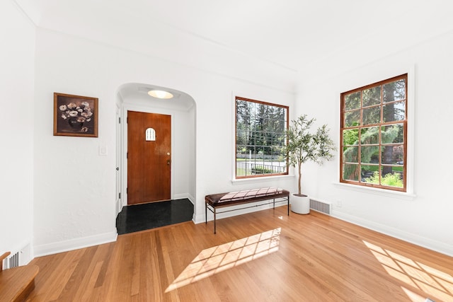 entryway with arched walkways, baseboards, wood finished floors, and visible vents