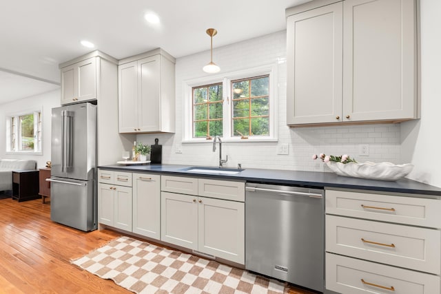 kitchen with decorative backsplash, dark countertops, appliances with stainless steel finishes, a sink, and light wood-style floors