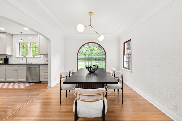 dining space with baseboards, a textured wall, light wood finished floors, and arched walkways