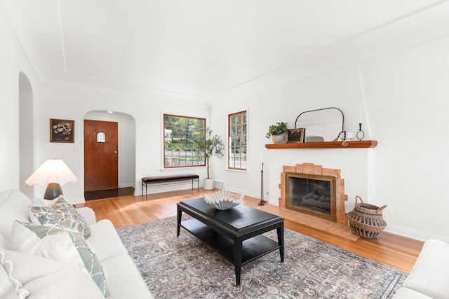 living area with a tiled fireplace, arched walkways, baseboards, and wood finished floors