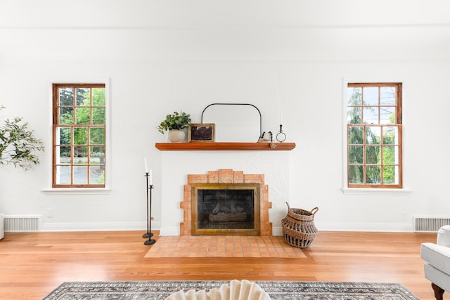 living room with baseboards, visible vents, a fireplace with flush hearth, and wood finished floors