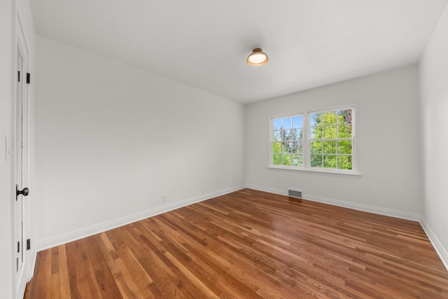 spare room featuring baseboards, visible vents, and wood finished floors