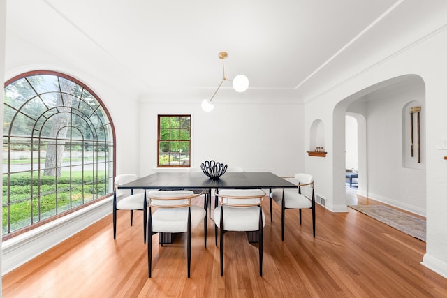 dining space featuring arched walkways, baseboards, visible vents, and light wood finished floors