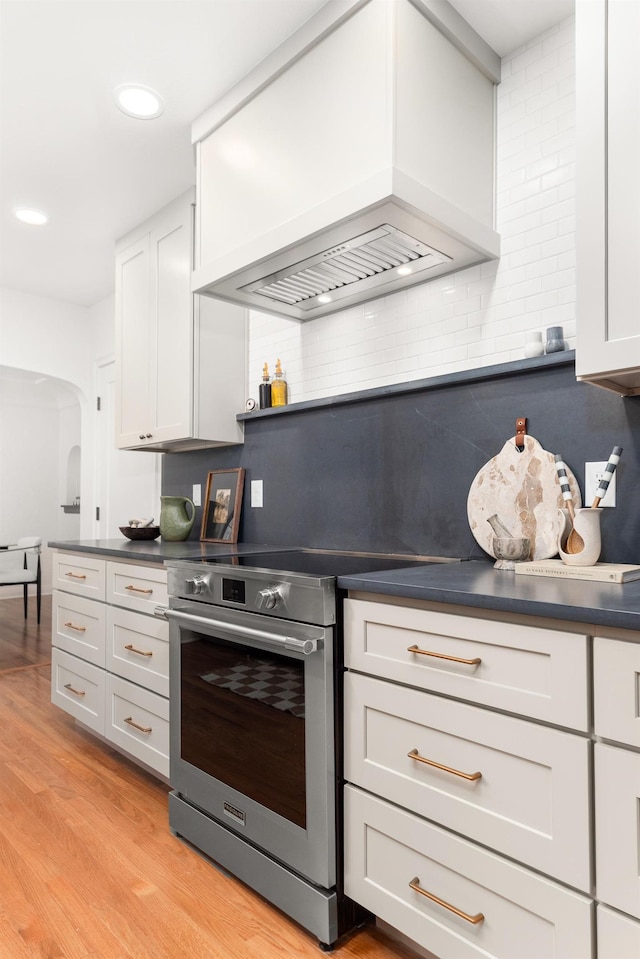 kitchen with decorative backsplash, dark countertops, premium range hood, arched walkways, and stainless steel range with electric cooktop
