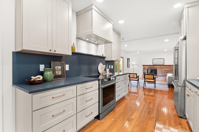 kitchen with dark countertops, appliances with stainless steel finishes, light wood finished floors, a fireplace, and custom range hood