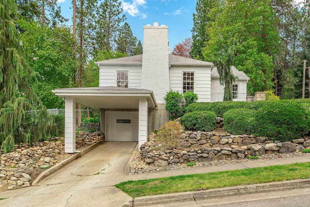 view of front of house featuring concrete driveway, a carport, a chimney, and a garage