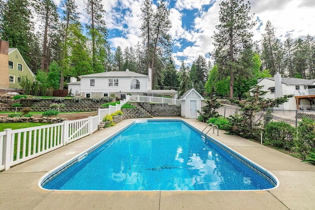 view of swimming pool featuring a shed, stairway, a fenced backyard, a fenced in pool, and an outdoor structure