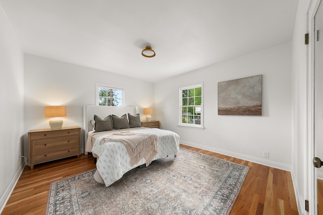bedroom with baseboards, multiple windows, and wood finished floors