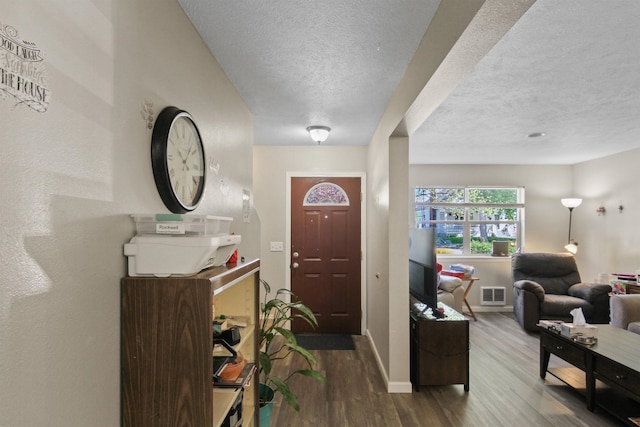 foyer featuring baseboards, a textured ceiling, visible vents, and wood finished floors